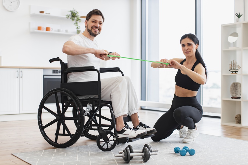 Female showing adult man in wheelchair how do exercises with stretching bands